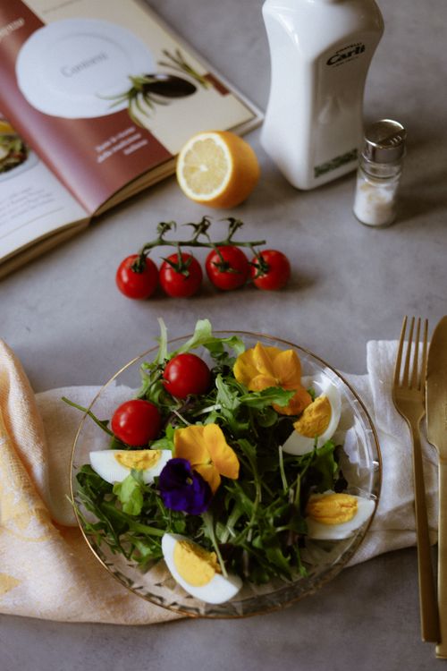 Free Leafy salad with tomatoes, edible flowers, and eggs on a table setting. Stock Photo