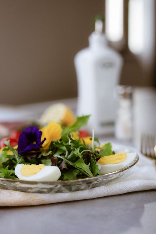 Free A vibrant salad with fresh greens, eggs, and edible flowers on a glass plate. Stock Photo