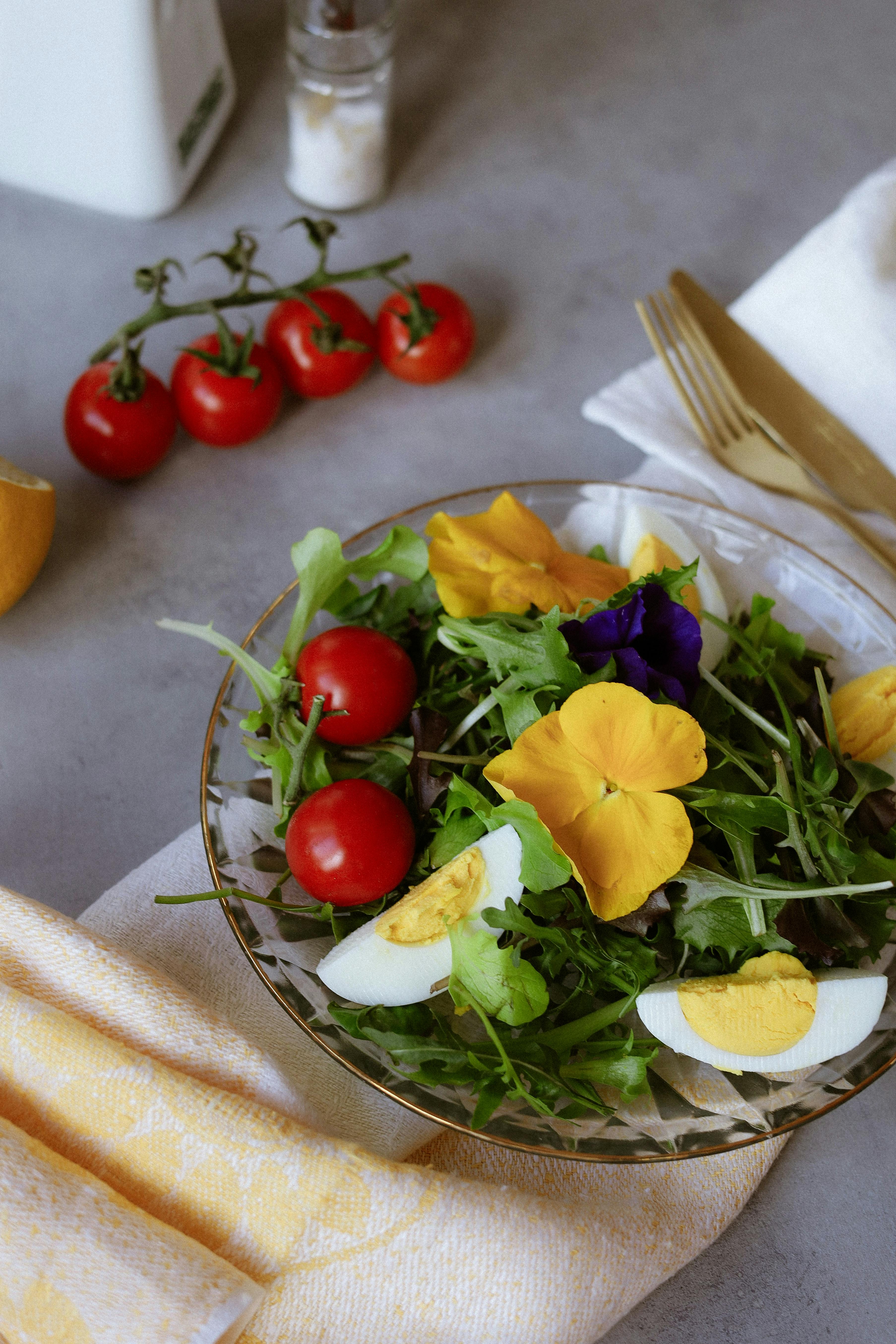 A colorful salad featuring cherry tomatoes, boiled eggs, and edible flowers on a table setting.