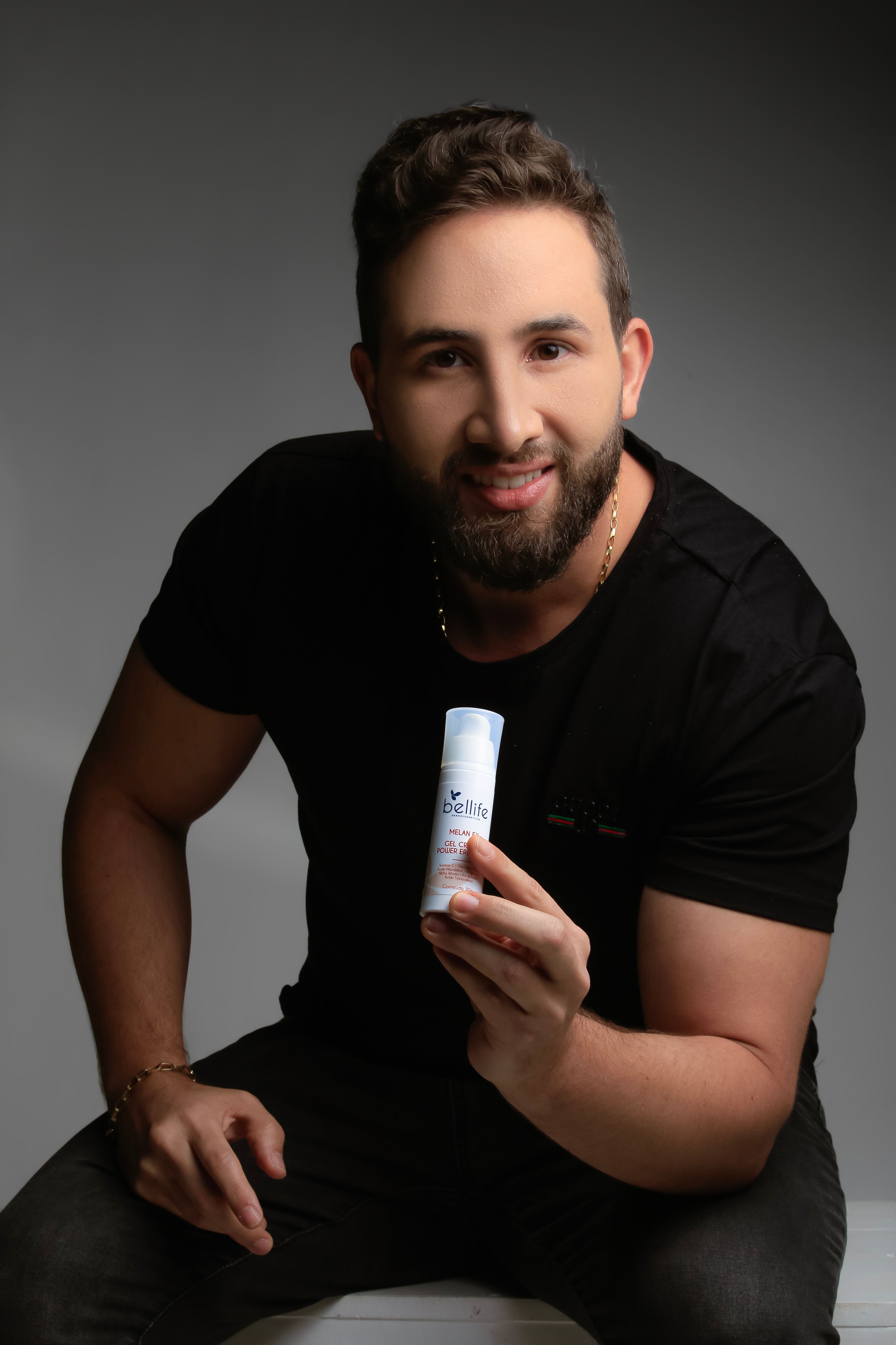 Adult man smiling and holding a skincare product in studio setting.