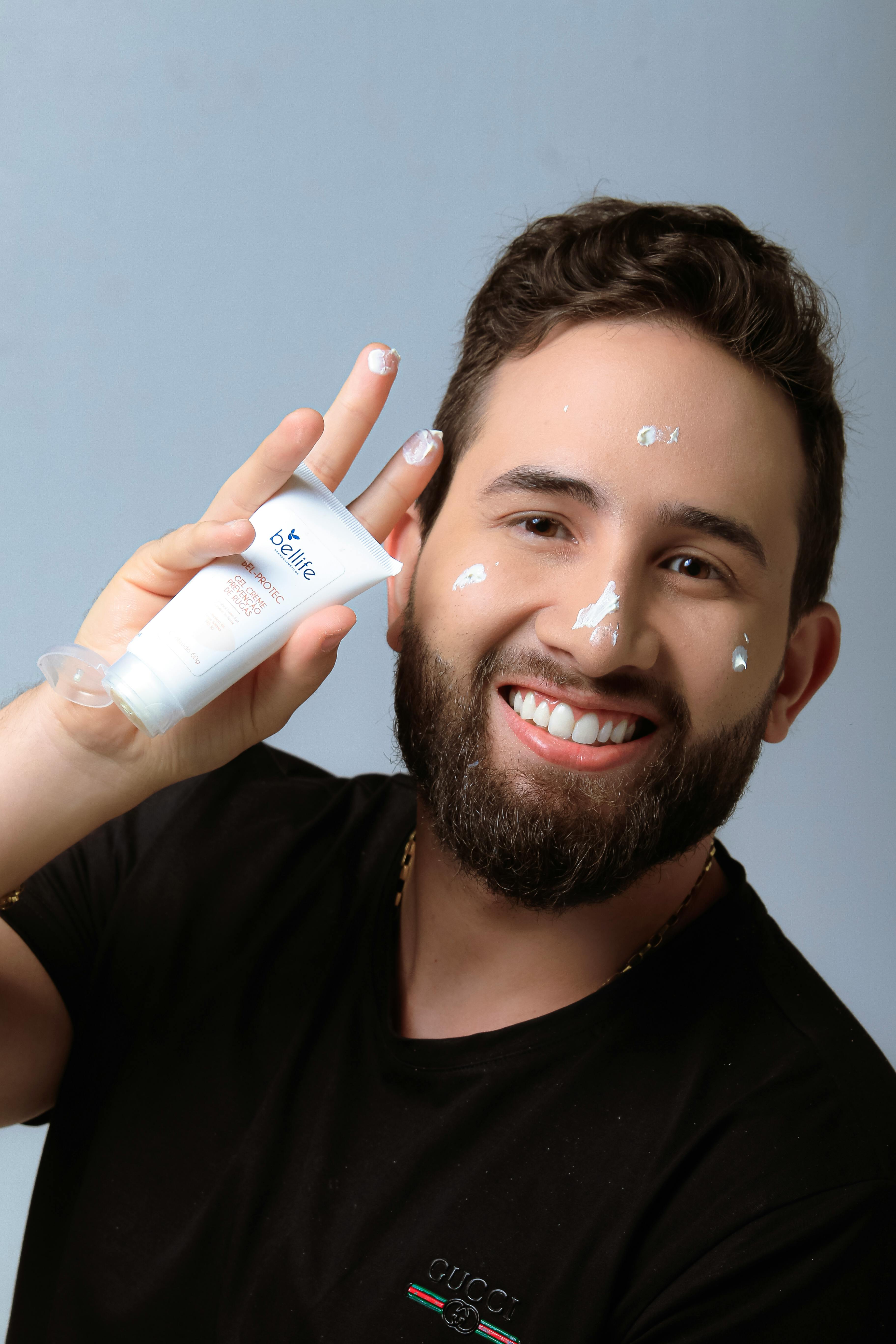 Portrait of a smiling man applying skincare cream. Promotes men's grooming.