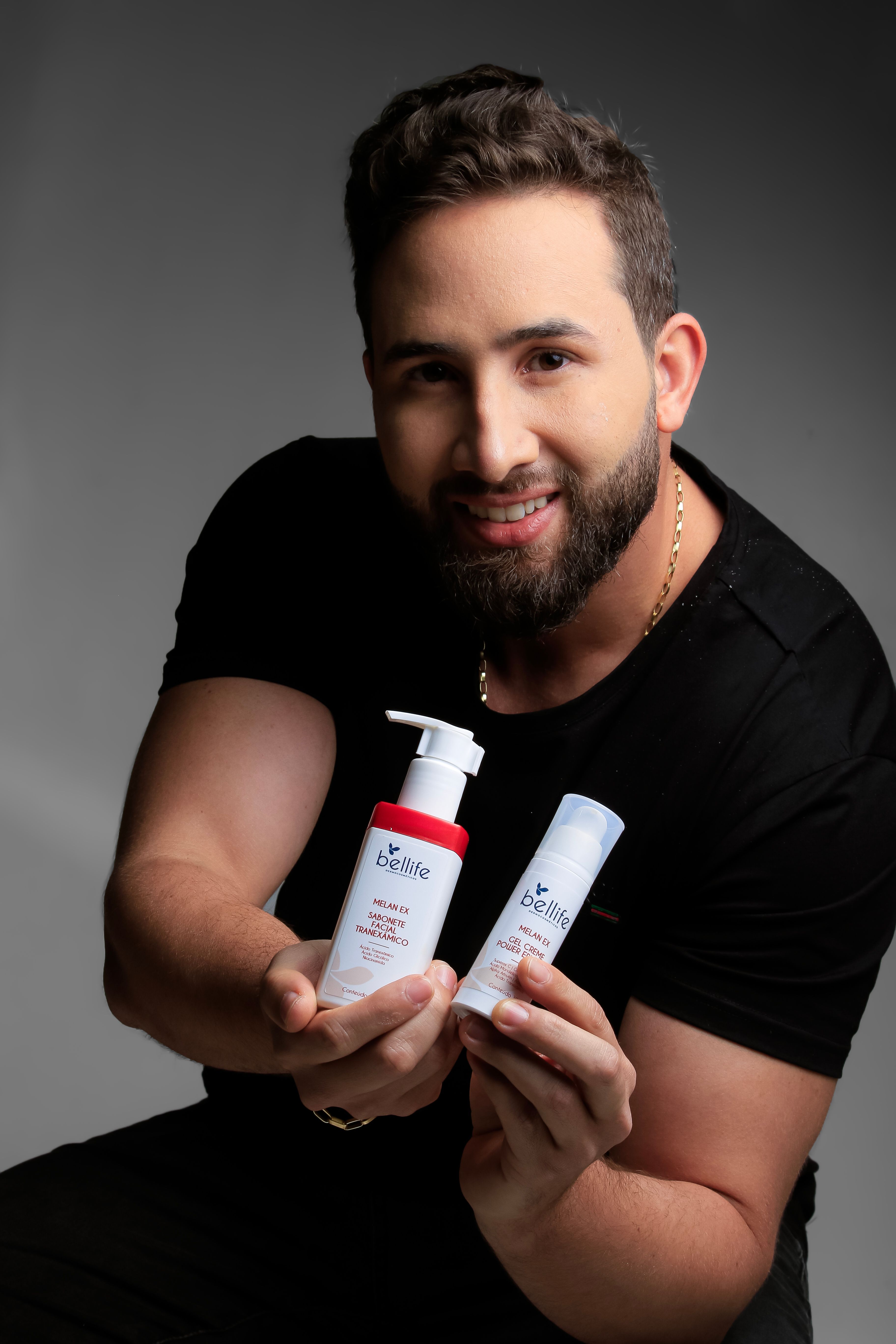 Young man holding skincare bottles, promoting cosmetics in a studio setting.