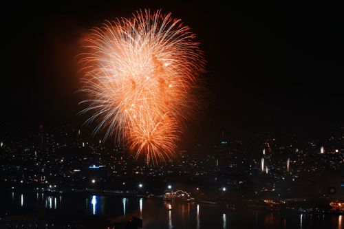 Free Stunning fireworks illuminating a bustling cityscape over water, creating a vibrant night scene. Stock Photo