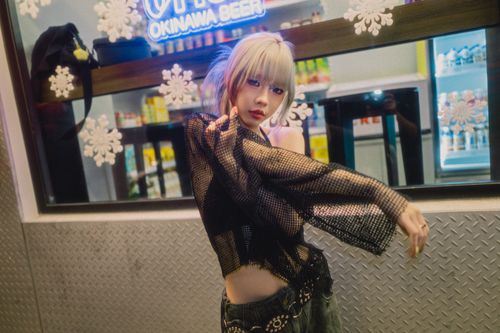 Free Fashionable woman in mesh top posing outside a city store with neon lights at night. Stock Photo