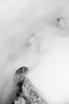 Aerial view of misty mountain peaks enveloped in clouds, captured in black and white.