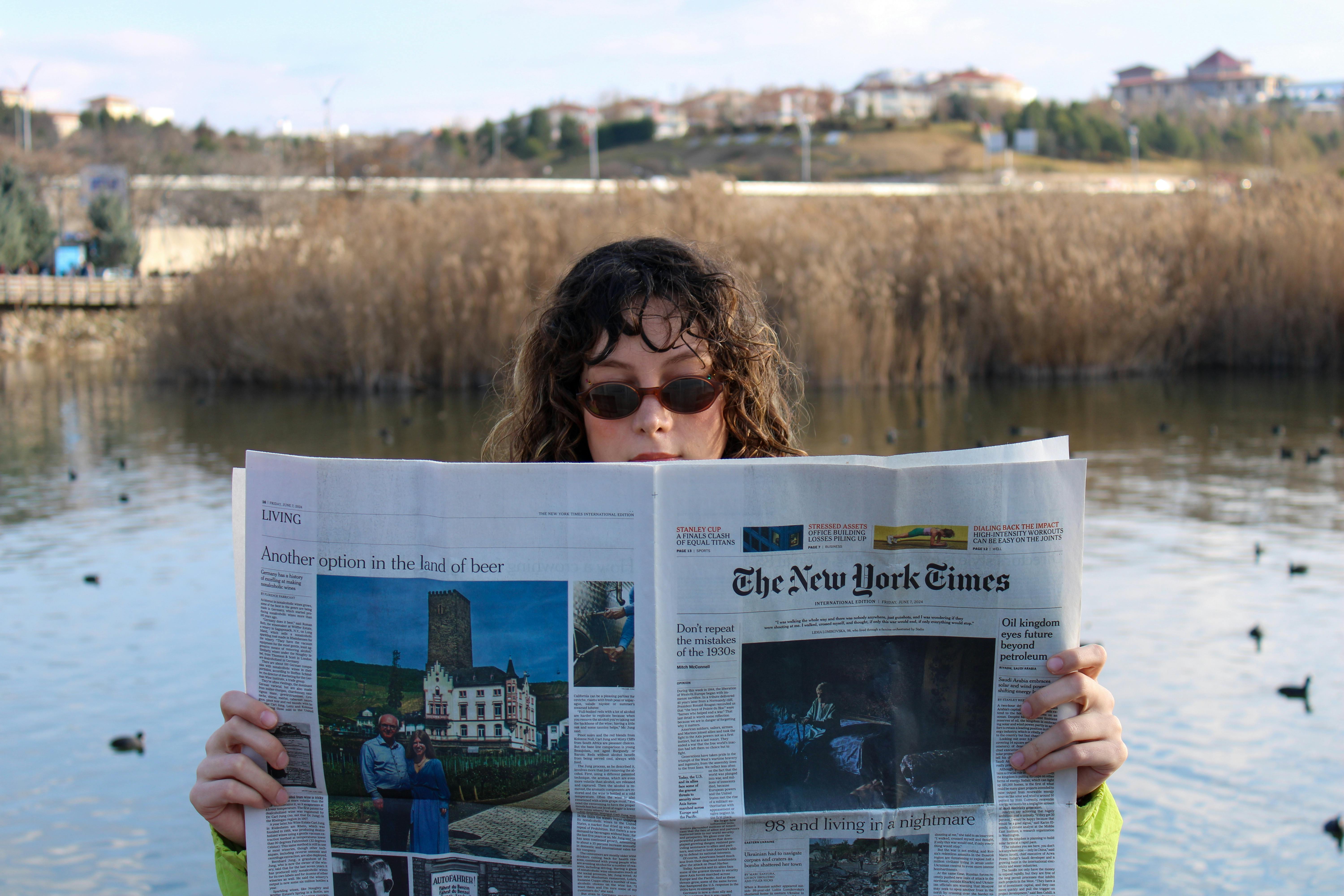 young woman reading newspaper by serene lake