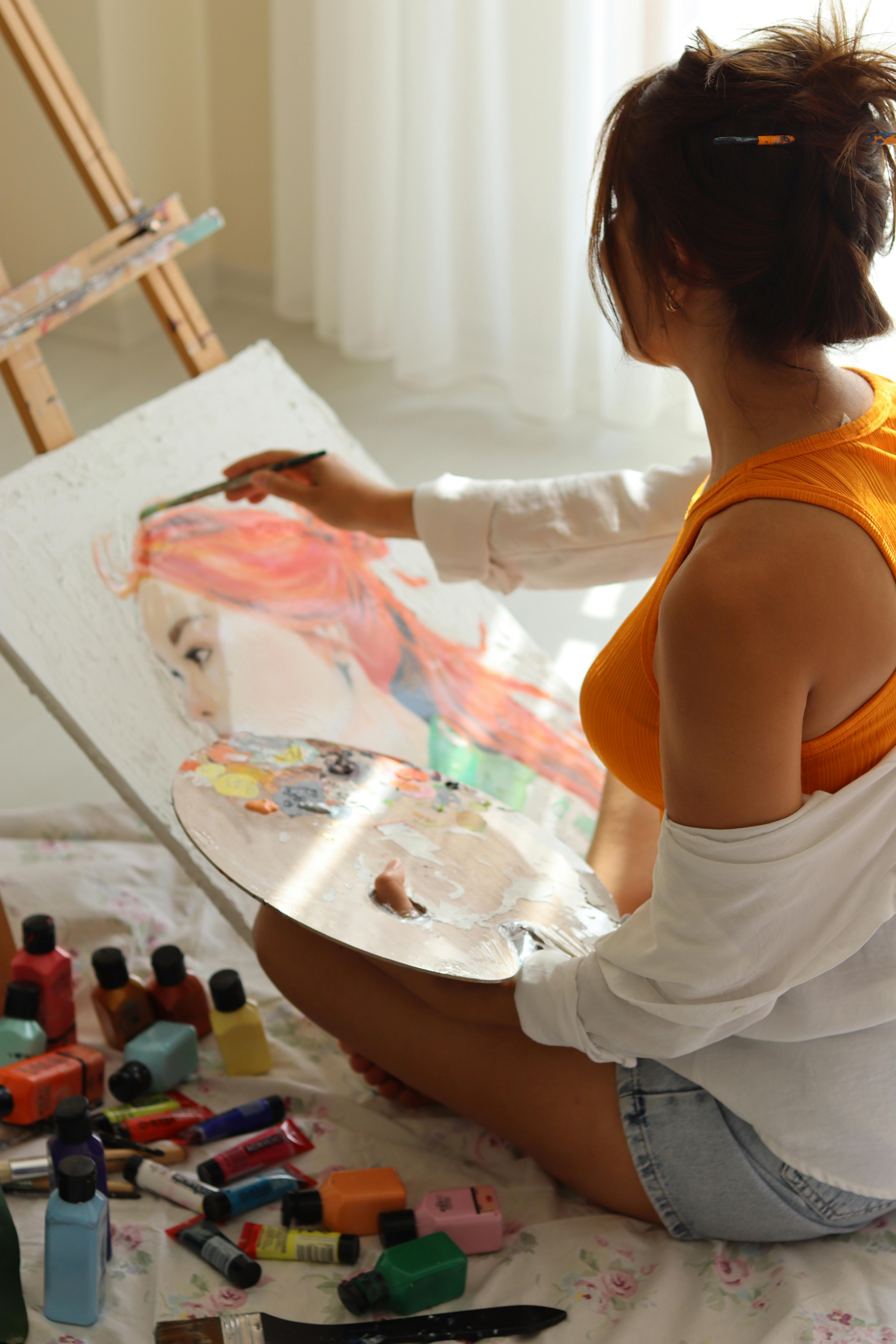 A young woman artist painting a portrait with vibrant colors in a sunlit room.