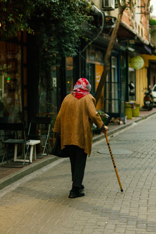 Free Elderly woman walks with cane down a quiet alley, evoking nostalgia. Stock Photo