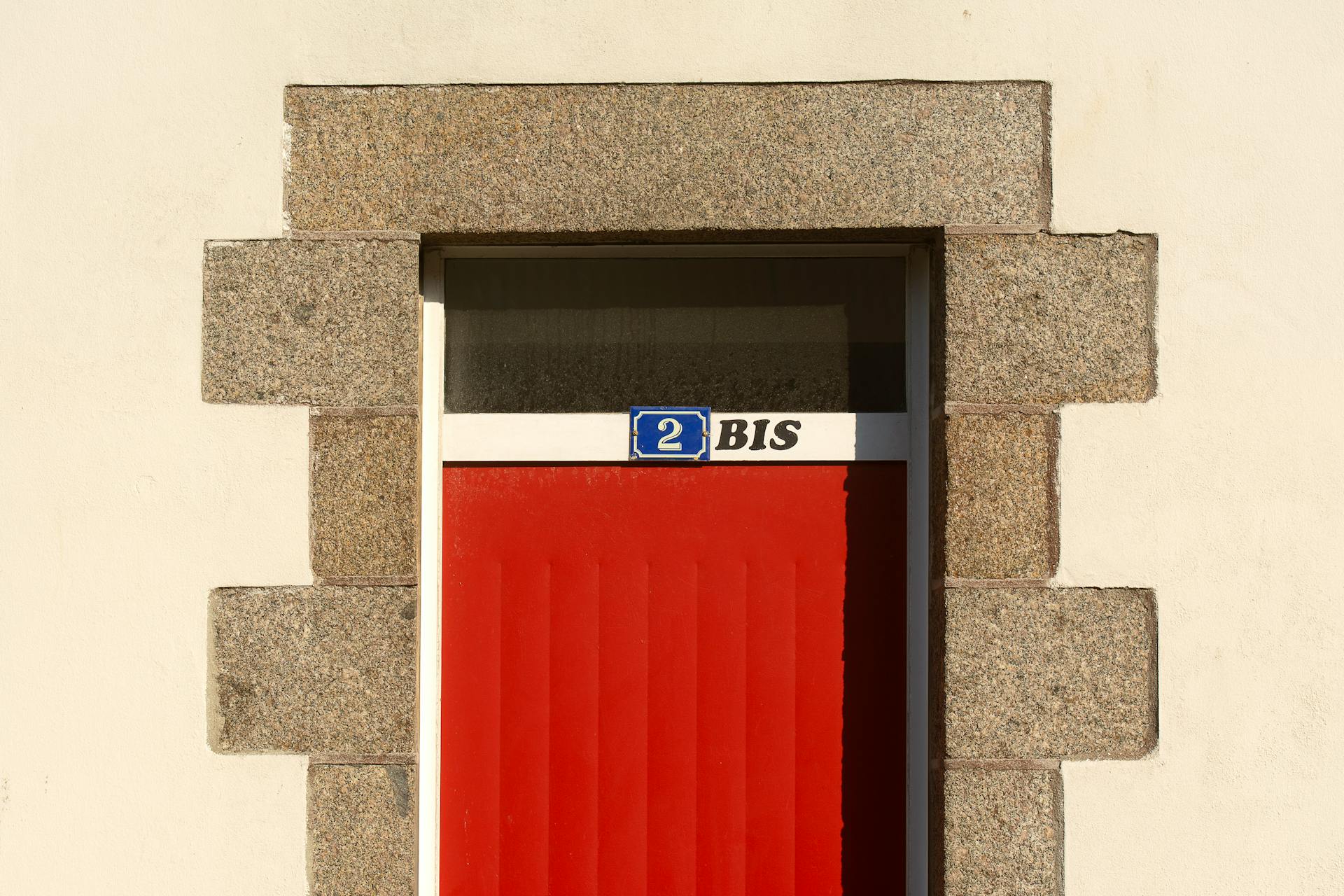 Close-up of a red door with number 2 BIS on a stone-framed building facade.