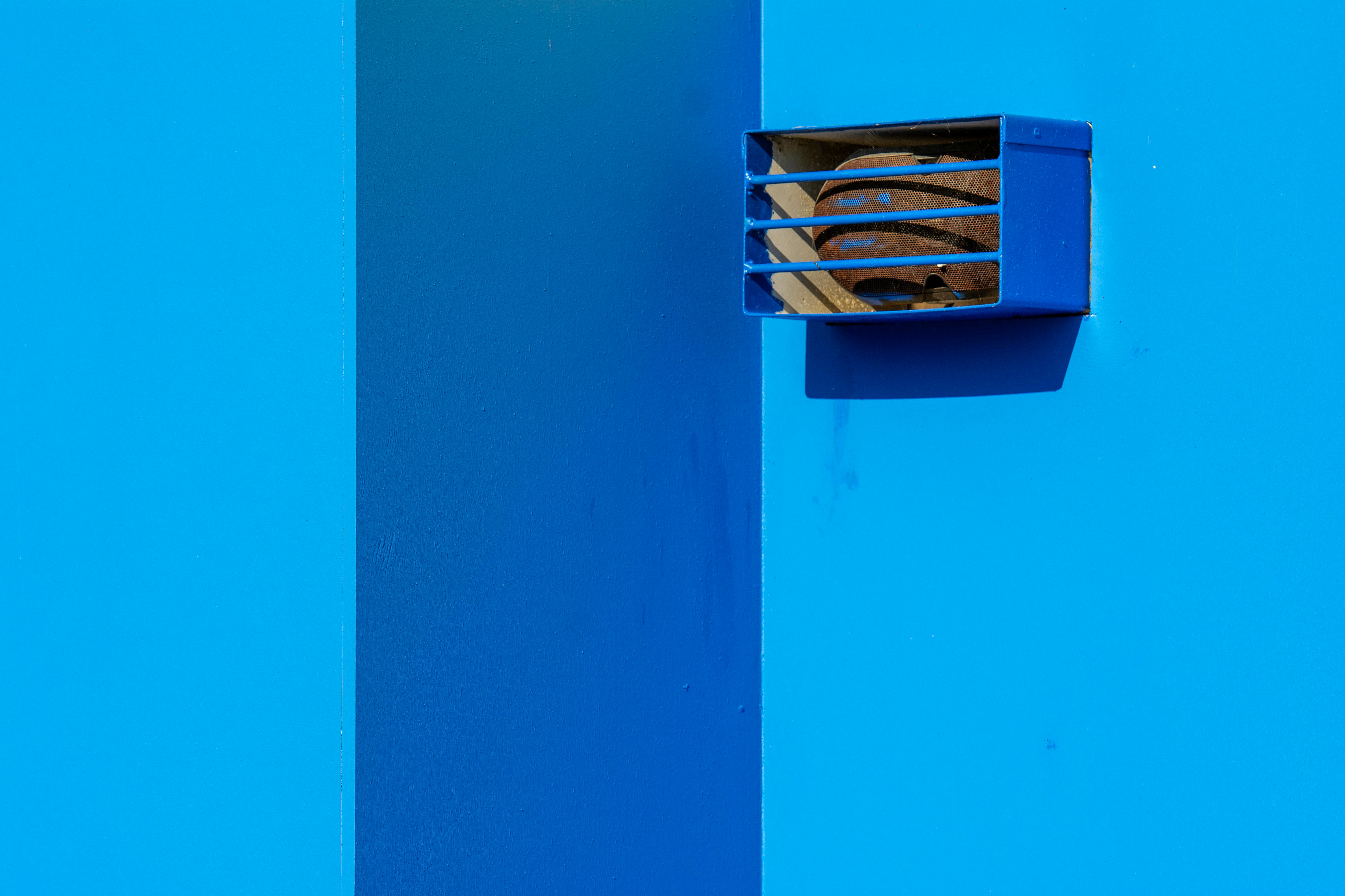 Zadarmo Minimalistický záber modrej steny s hrdzavým prieduchom za slnečného dňa, ktorý zvýrazňuje geometrickú jednoduchosť. Fotka z fotobanky