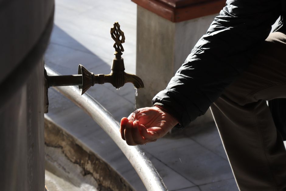 A close-up of a hand under a dripping, decorative outdoor tap. Perfect for water conservation themes.