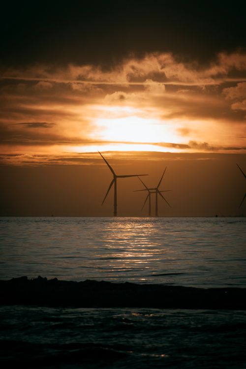 Free Scenic view of wind turbines at sea against a dramatic sunset sky. Stock Photo