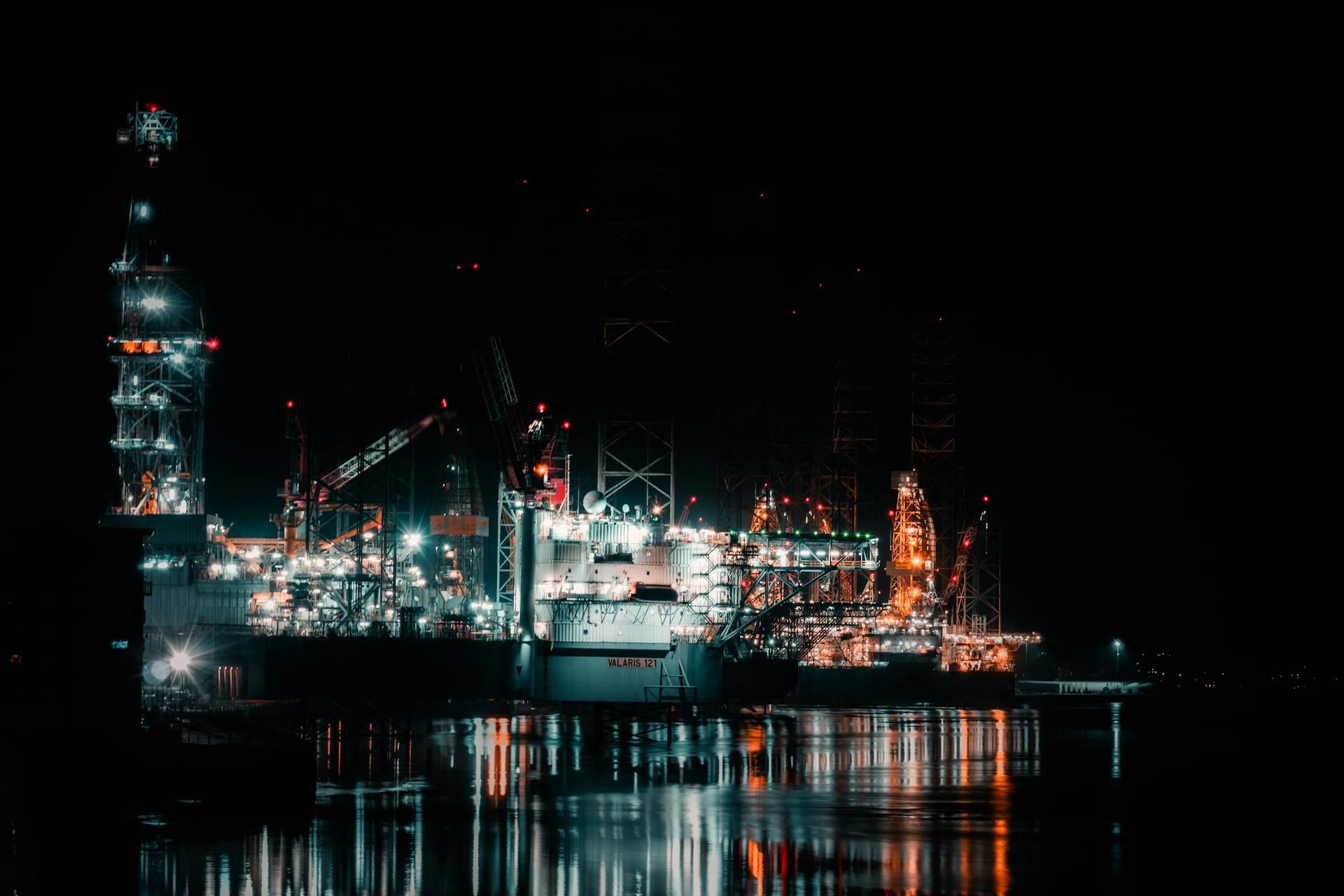 Night view of a brightly lit offshore oil rig reflecting on water. Industrial elegance.