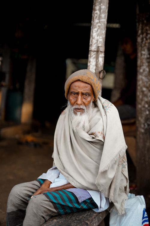 Free A poignant portrait of an elderly man in traditional attire seated outdoors, capturing his thoughtful expression. Stock Photo
