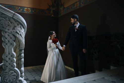 Free Couple in wedding attire holding hands in a beautifully decorated staircase. Stock Photo
