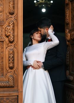 A bride and groom embrace lovingly in an intricately carved wooden doorway, symbolizing love and togetherness.