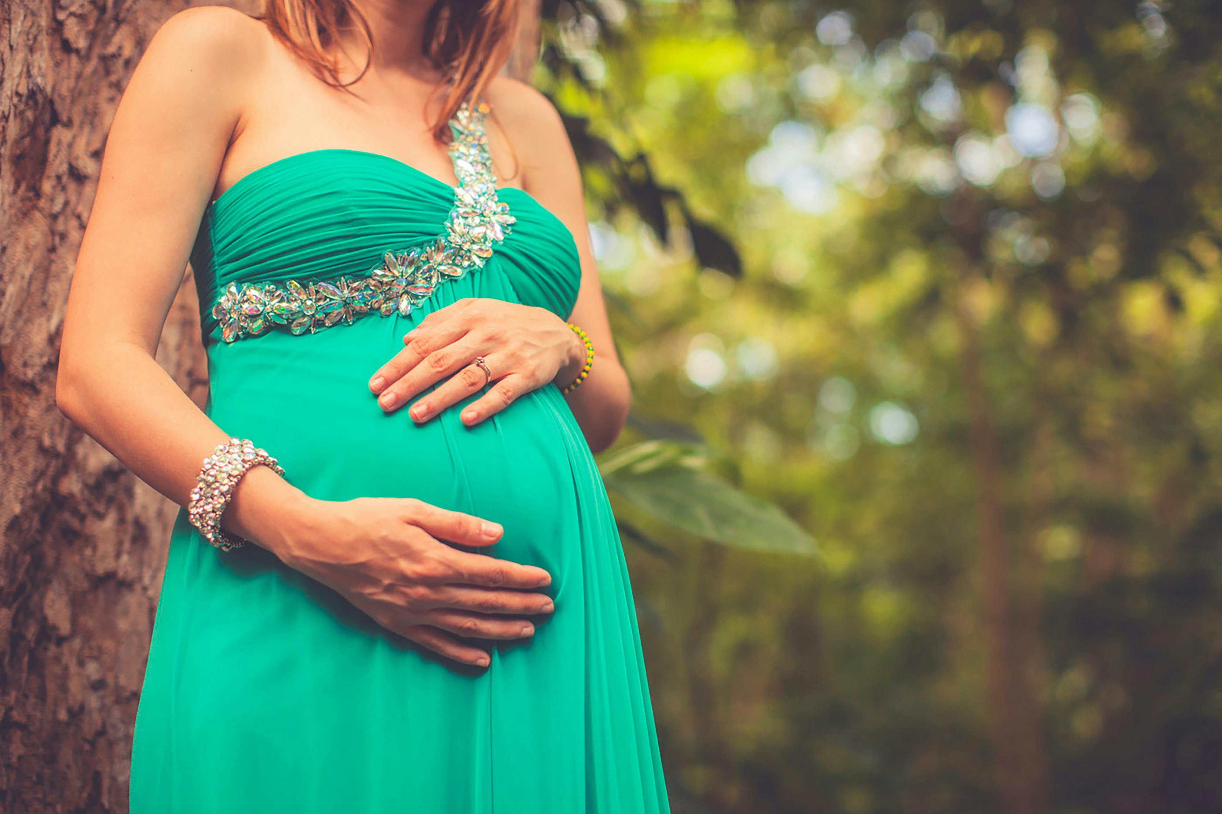 pregnant woman in green one shoulder dress holding her belly