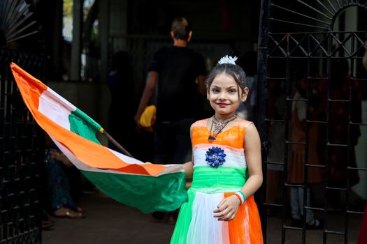 Smiling girl in tricolor dress holds Indian flag during Independence Day celebration in India.