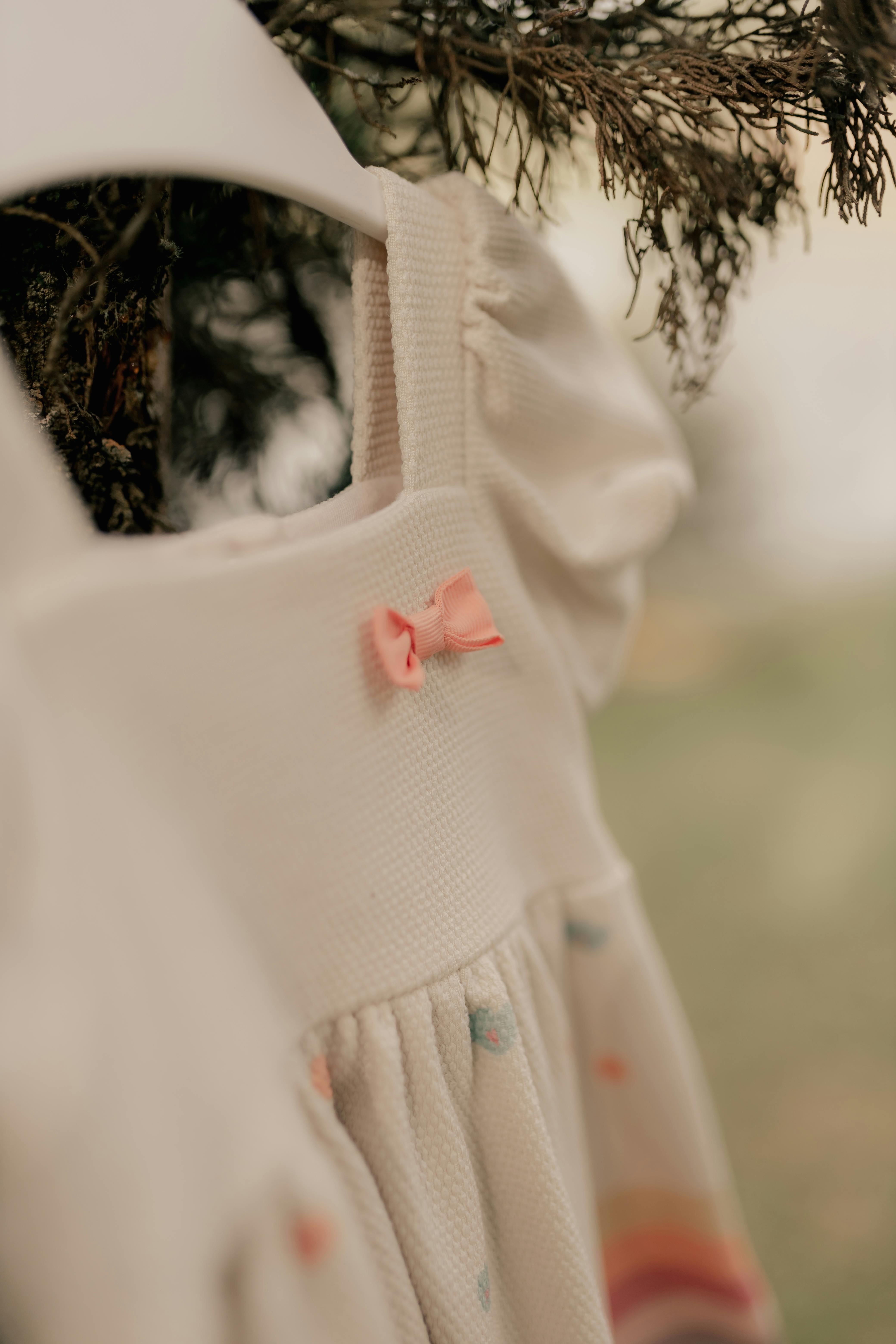 Soft focus on a cute baby dress with pink bow hanging on a tree branch outdoors.
