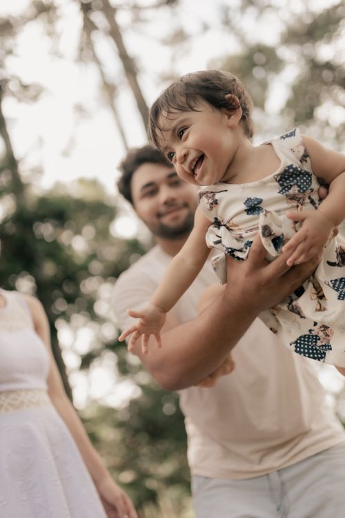 Free Father joyfully lifting smiling baby girl outdoors. Happy moment in a natural setting. Stock Photo
