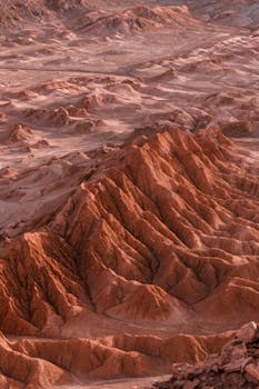 Explore the intricate patterns of desert dunes and mountains in this breathtaking aerial shot.