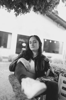 A relaxed woman sitting outdoors in a black and white portrait, exuding confidence.