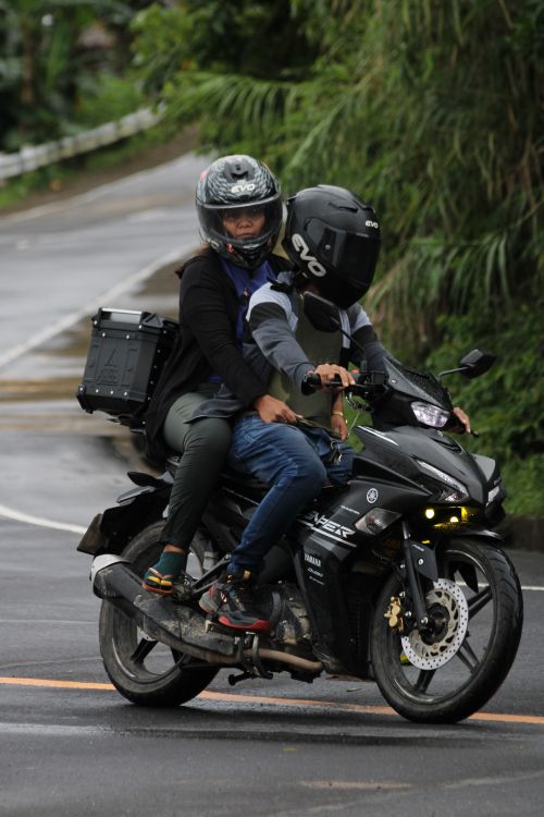 Free Two individuals wearing helmets riding a motorcycle on a rainy road. Stock Photo