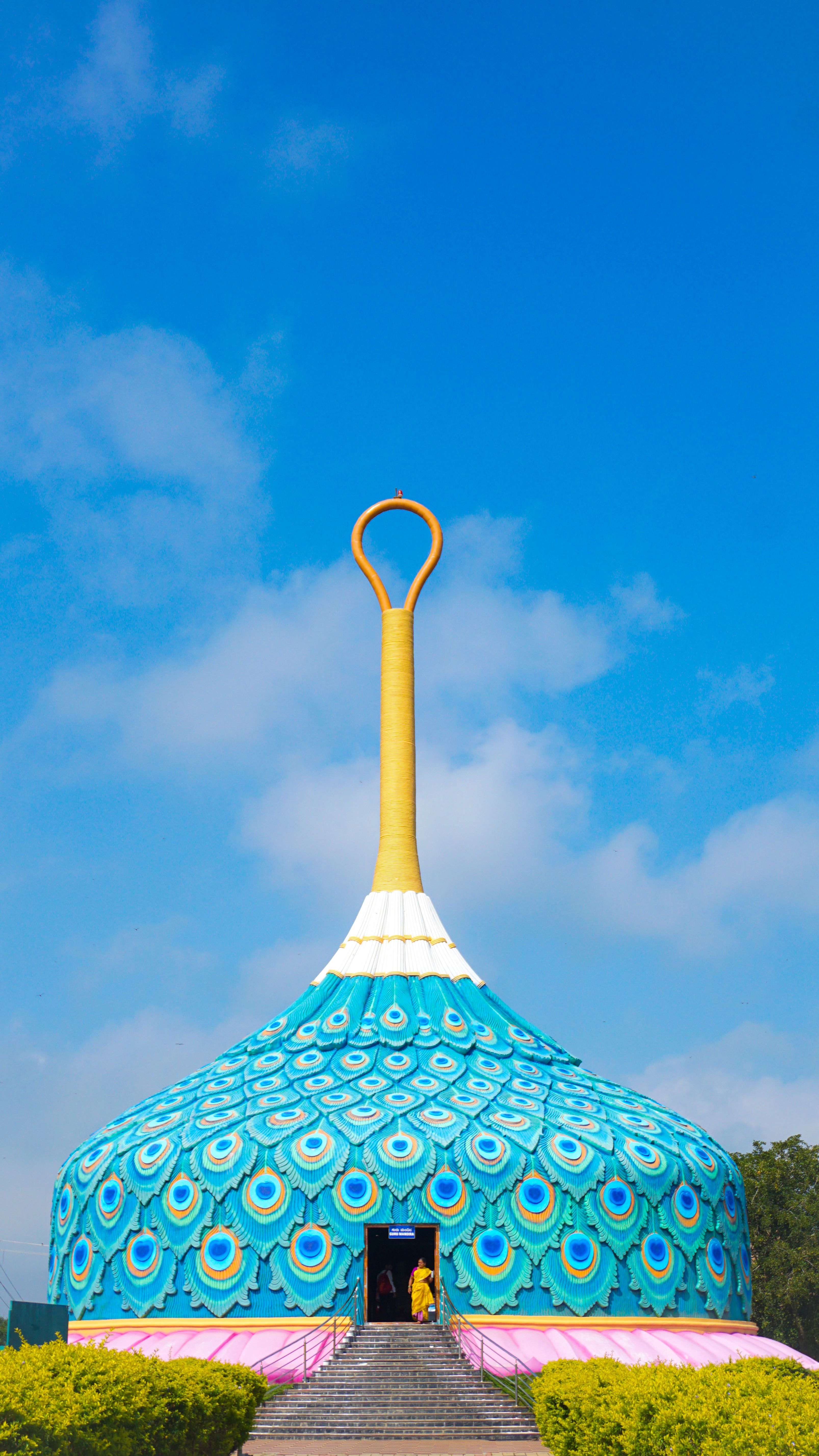 A vibrant peacock-inspired temple structure set against a clear blue sky.