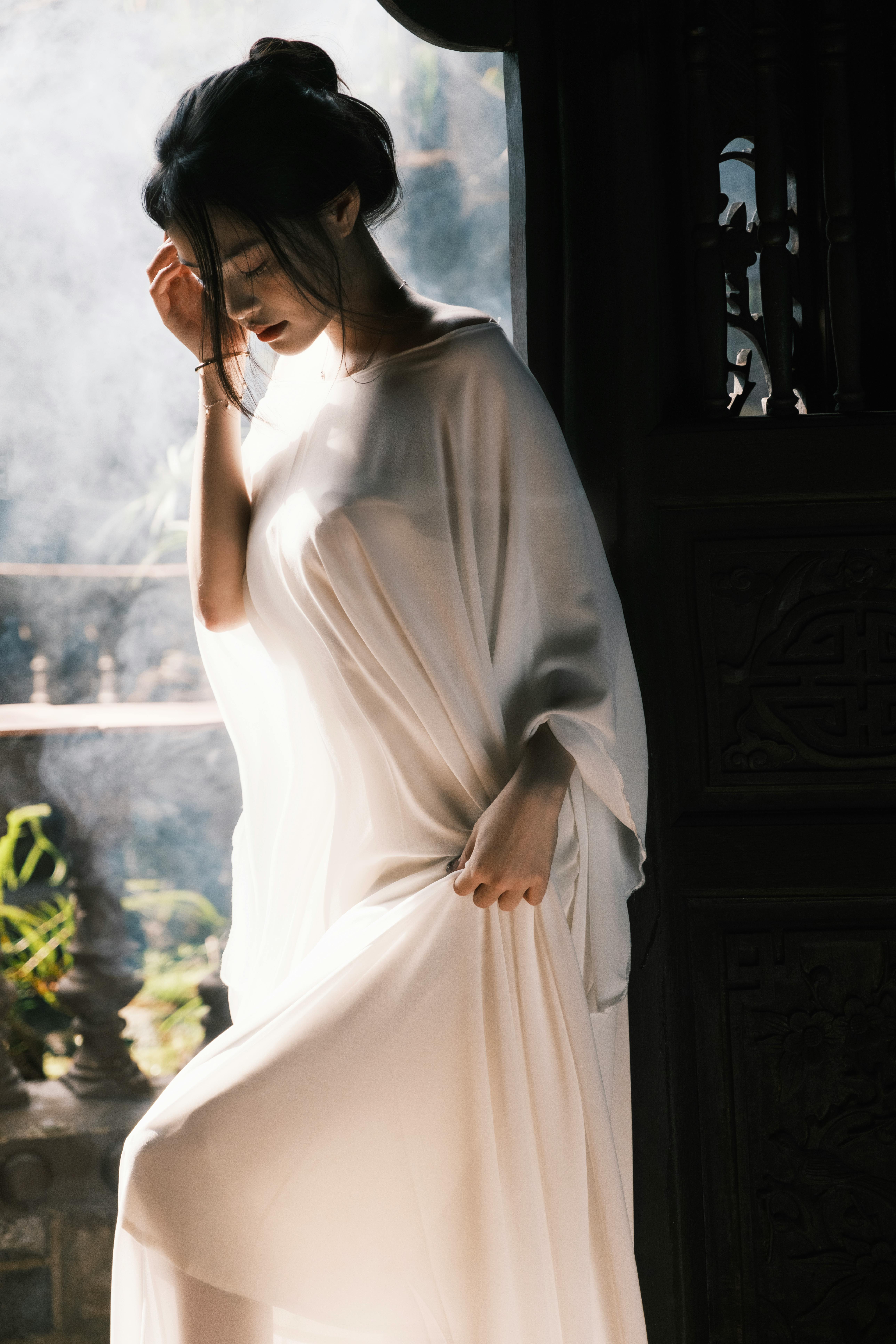 Elegant woman in white dress illuminated by natural light, evoking calm and grace.