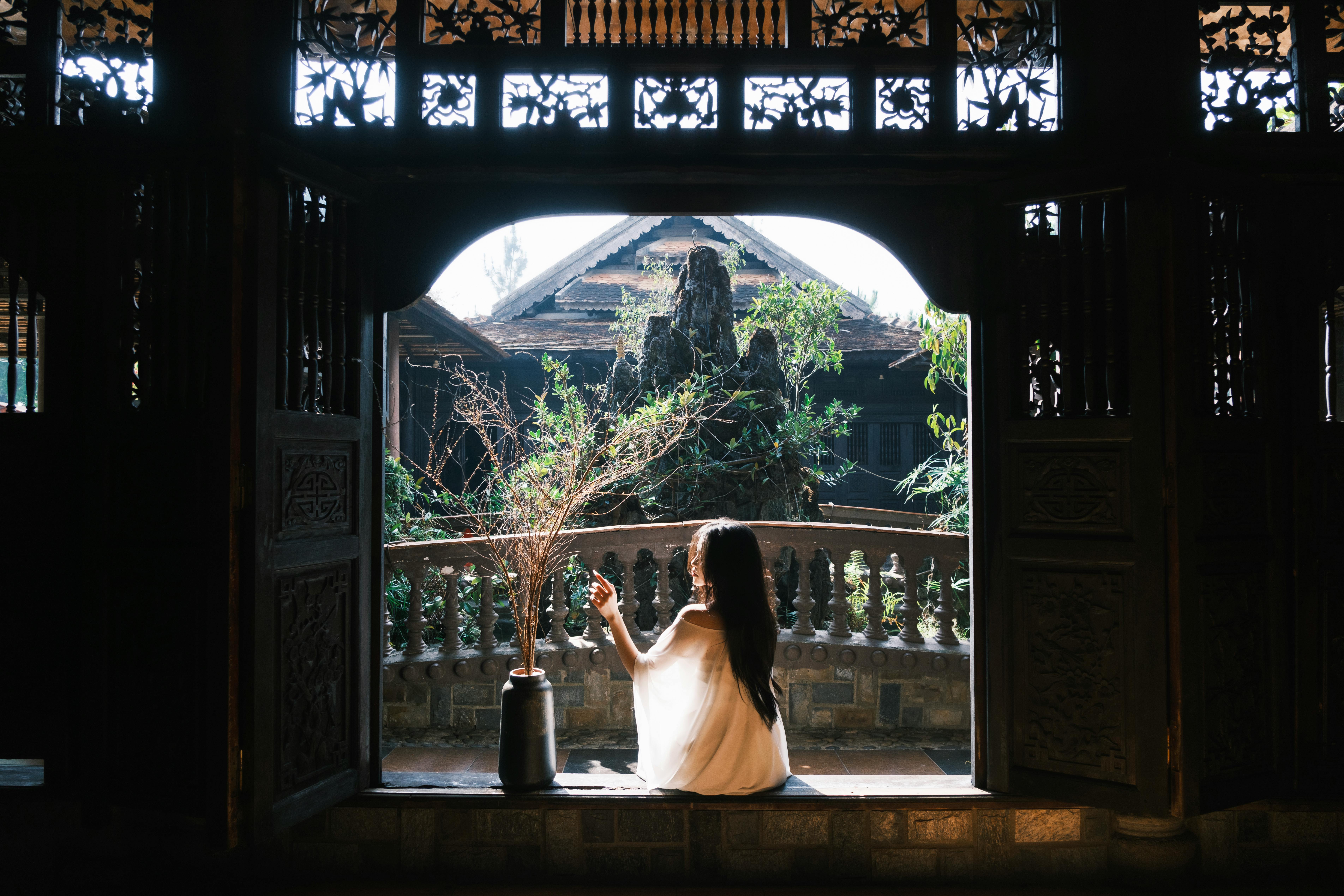 A woman sits inside a traditional building, gazing outdoors.