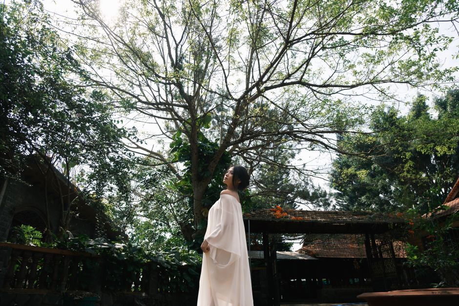 Woman standing in peaceful garden under sunlit trees, embracing nature.