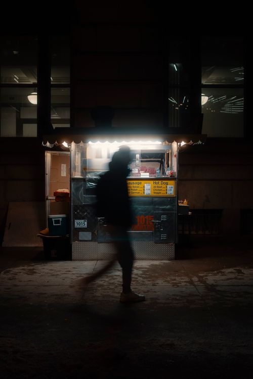 Free Silhouetted person passes by an illuminated street food cart at night. Stock Photo