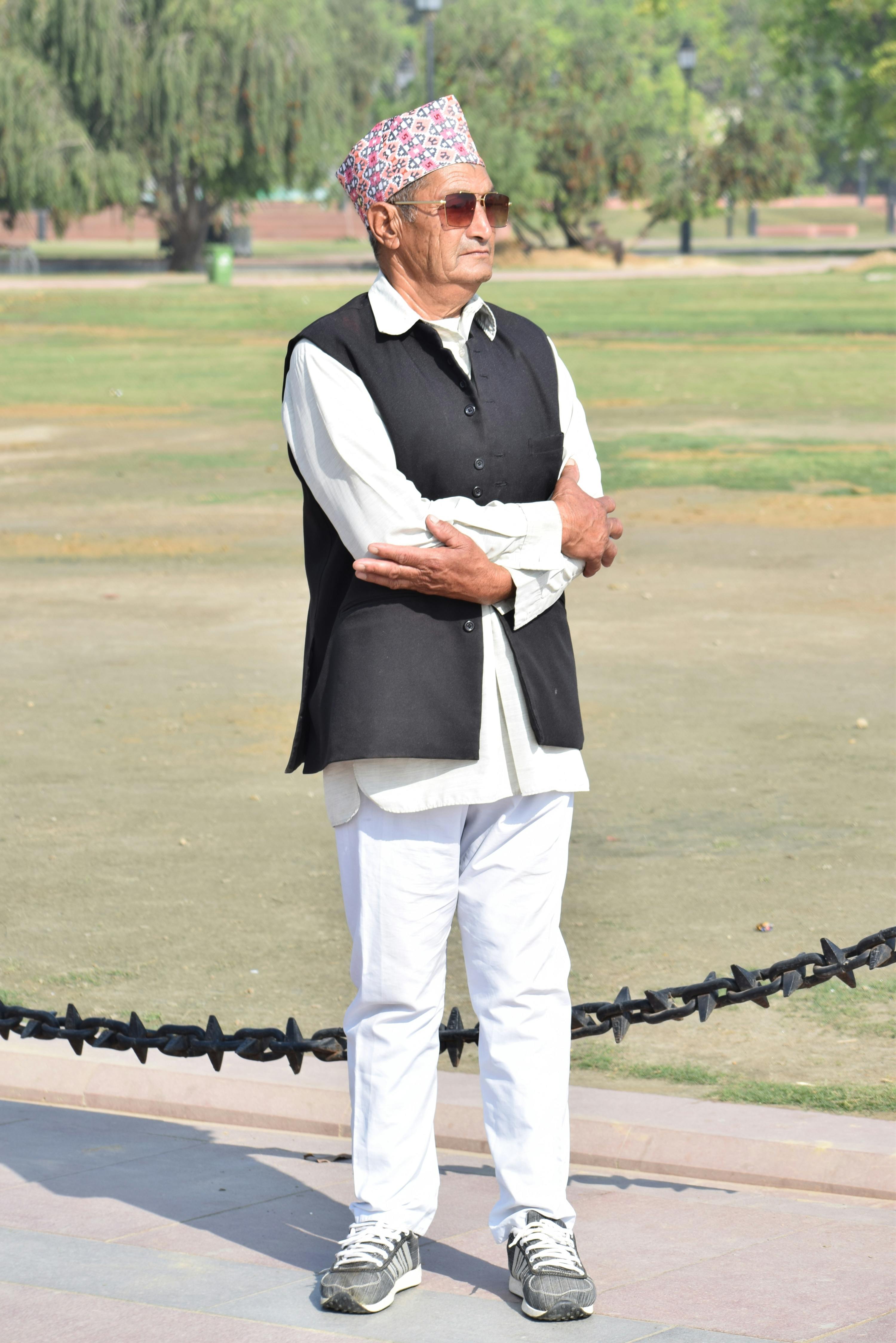 Elderly man in traditional dress standing outdoors on a sunny day.