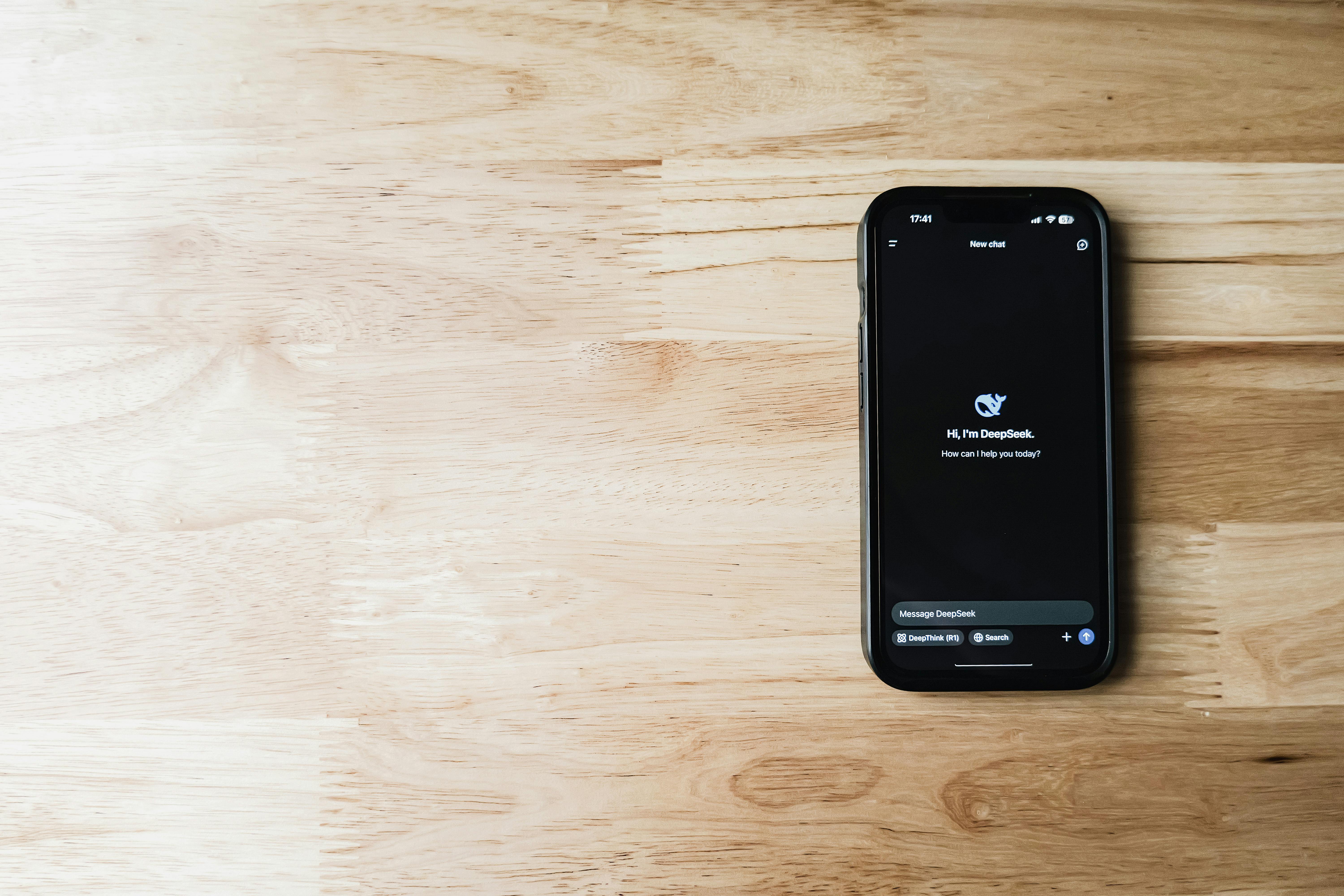 Free A smartphone featuring an AI assistant app, placed on a light wooden table, showing tech and communication. Stock Photo