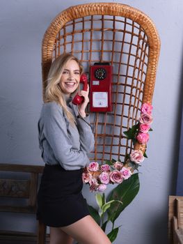 Smiling woman talking on a vintage red phone with rose decorations.