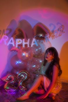 Woman posing with colorful balloons and soft colorful lighting.
