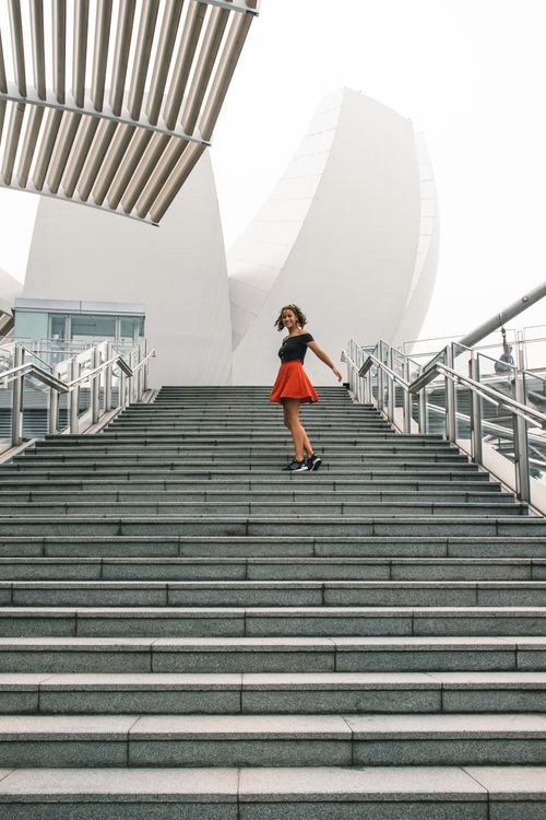 Free A woman in a red skirt stands on stairs outside the iconic ArtScience Museum in Singapore. Stock Photo