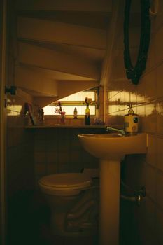 A compact bathroom under stairs with warm lighting and decor.