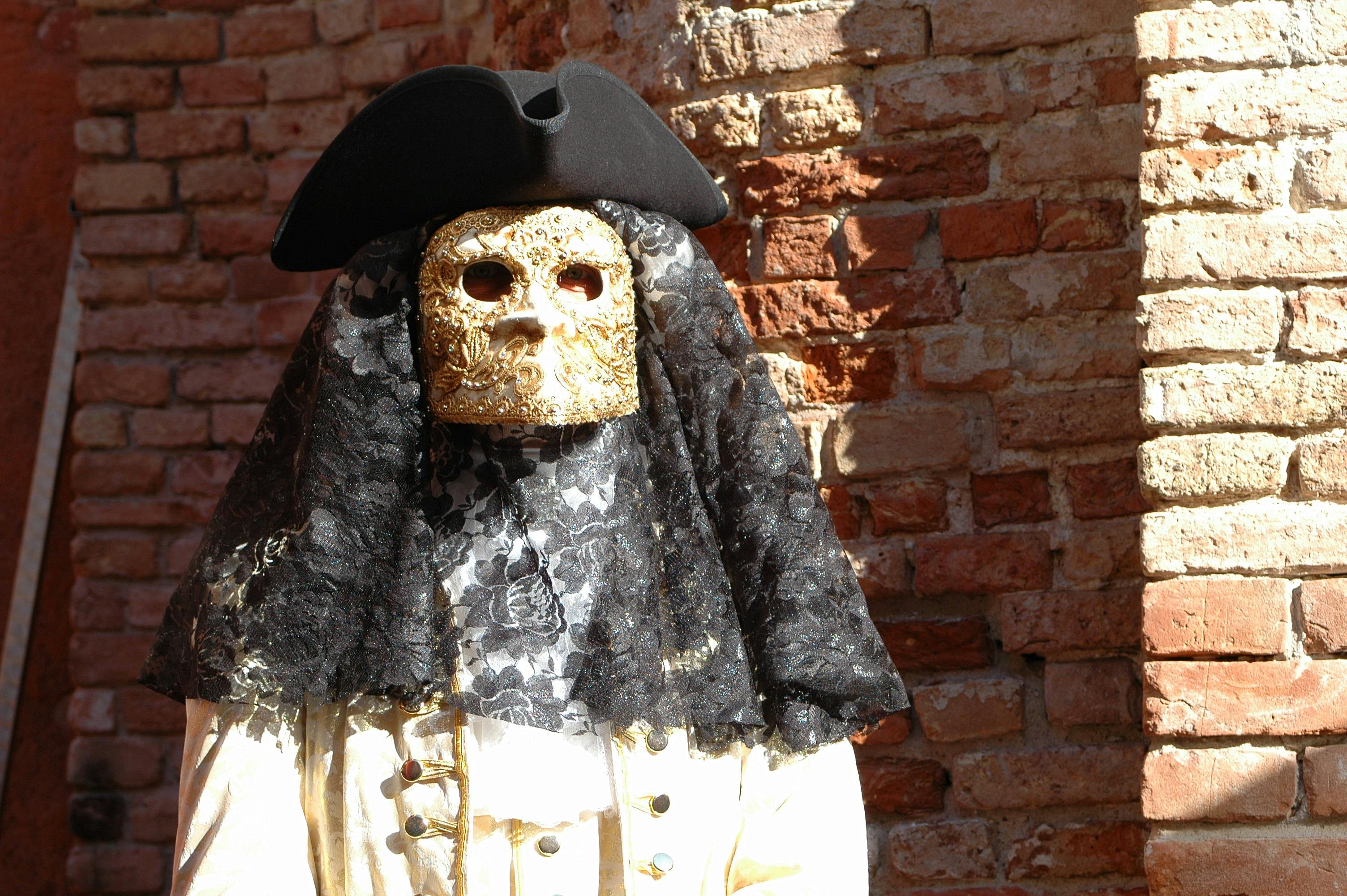 Free A person in a traditional Venetian mask and costume against a brick wall. Stock Photo