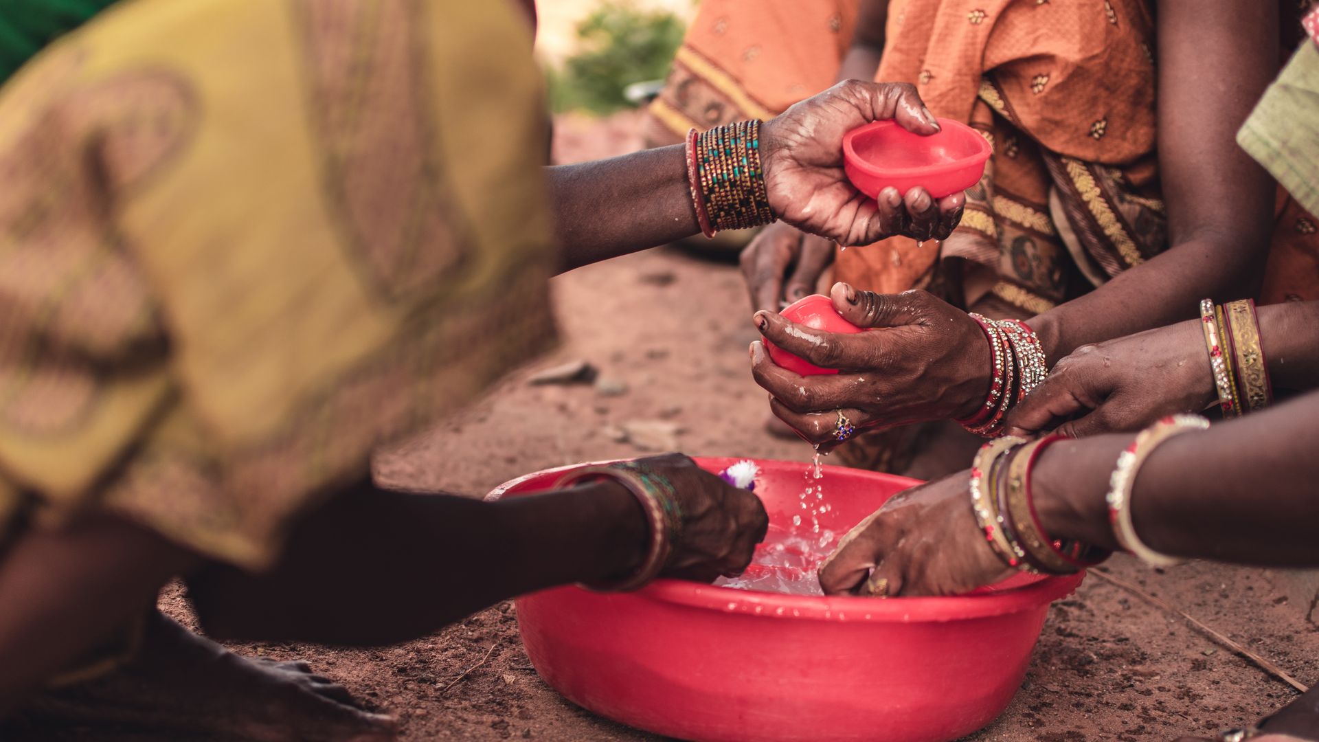 People Washing Their Hands in a Round Red Plastic Container