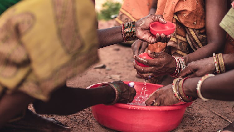 People Washing Their Hands In A Round Red Plastic Container