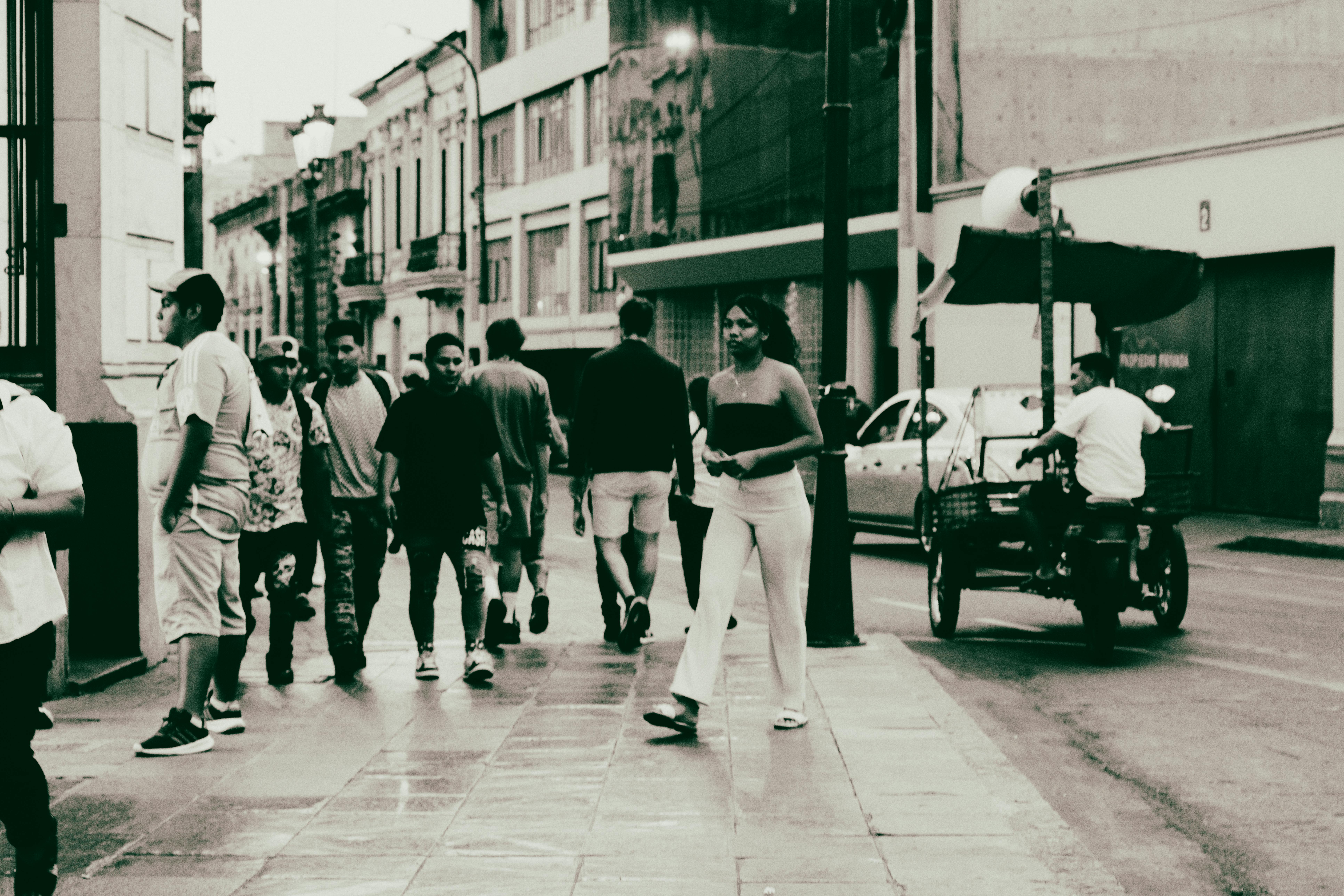 Busy city street featuring pedestrians and a tuk-tuk at dusk, showcasing urban life.