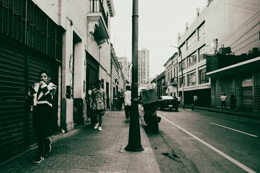 Black and white urban street scene with people walking, cars, and buildings.