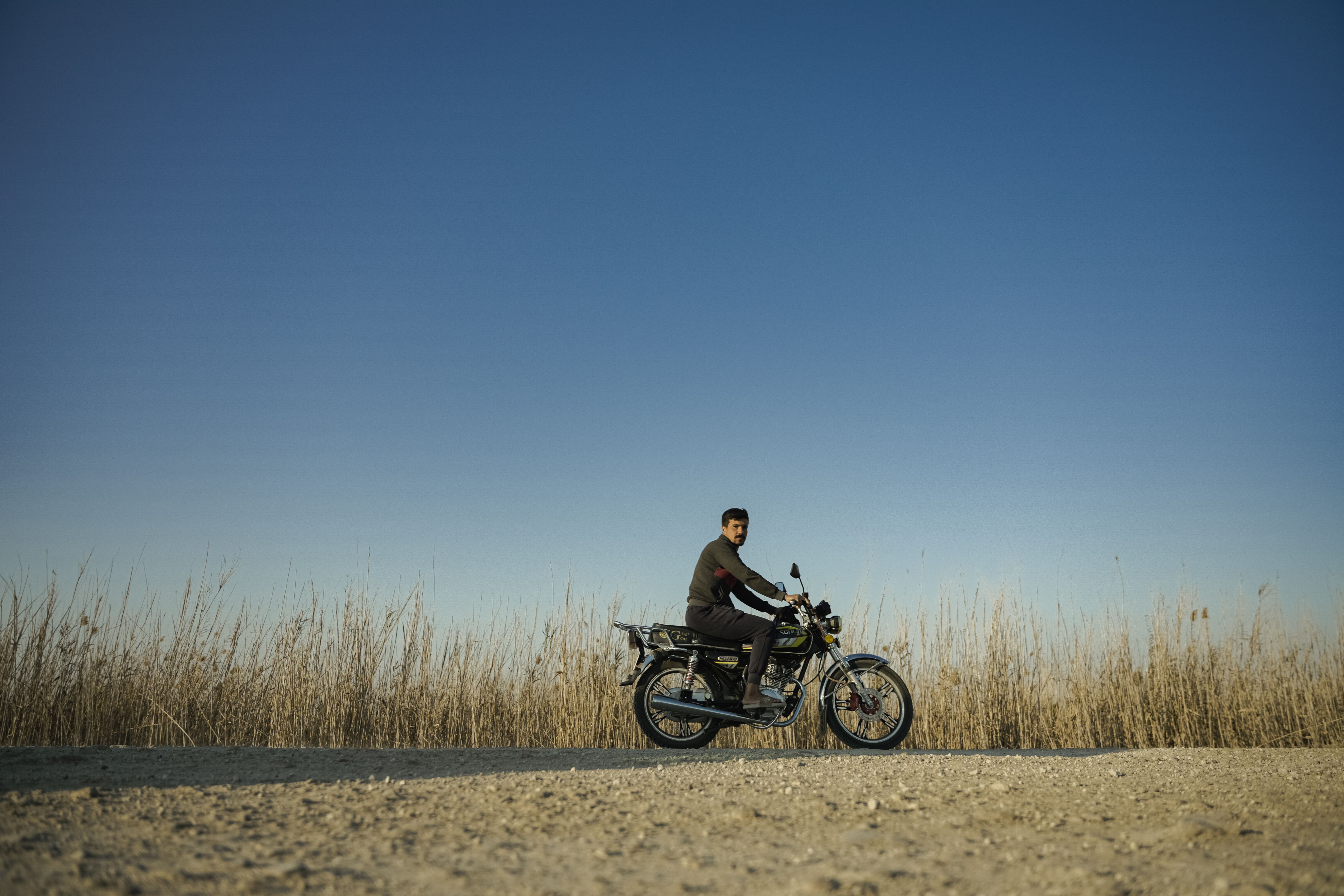 Man riding a motorcycle on rural road under blue sky · Free Stock Photo