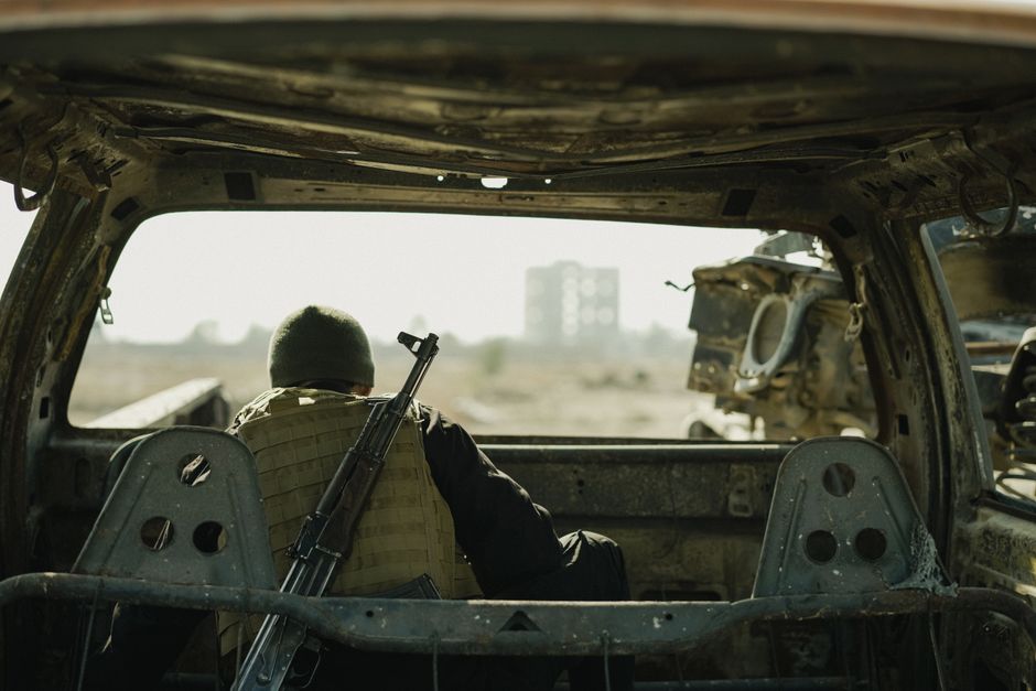 Beyond Backups: Advanced Ransomware Protection Strategies 4 - Beyond Backups,Advanced Ransomware Protection For Small Architecture Firms - - Bonelli Systems A Soldier In A Vest Sits In An Abandoned Vehicle, Observing A Distant Building.