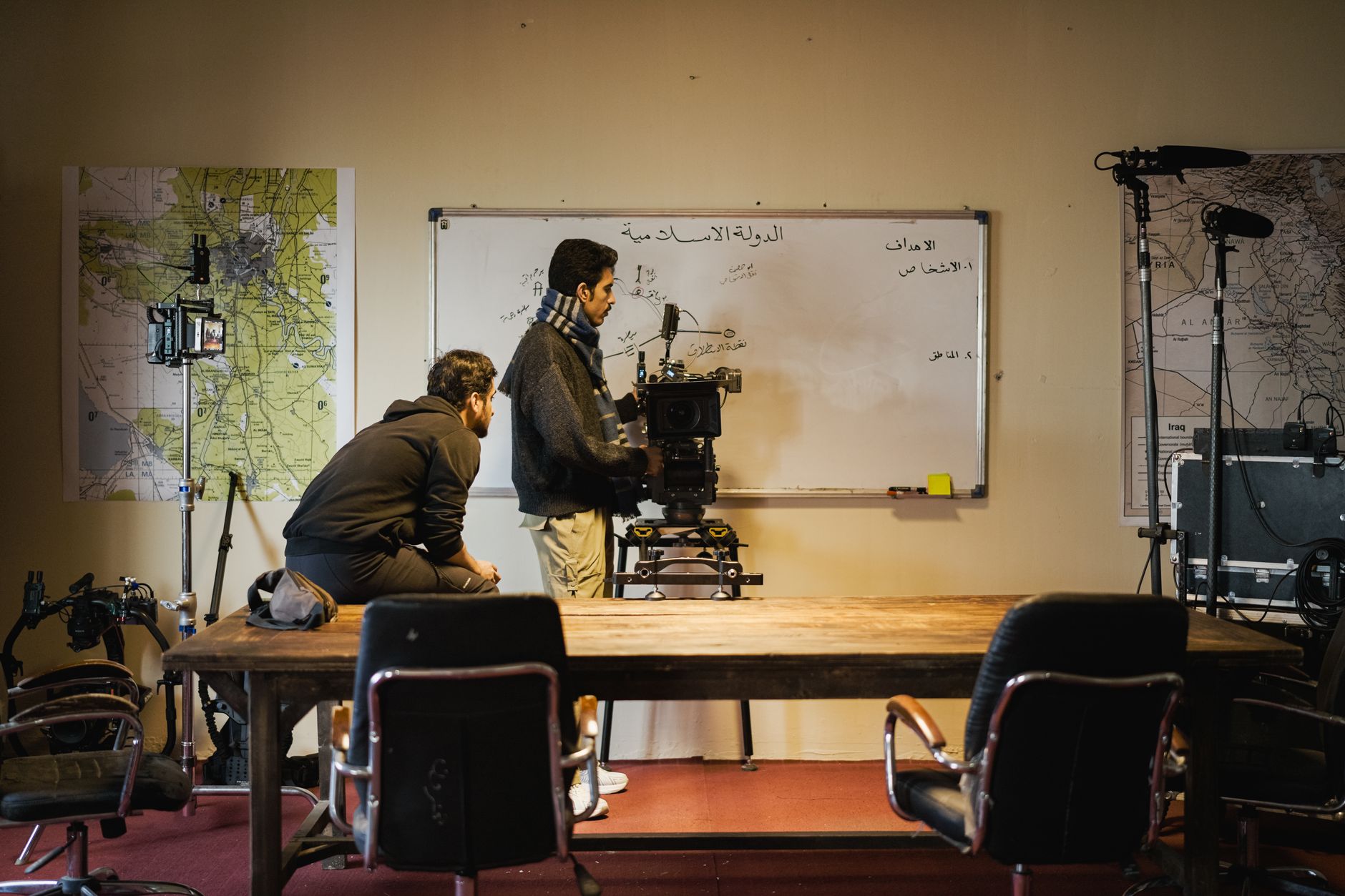 Two men setting up a camera in an indoor film studio. Maps and equipment surround them.