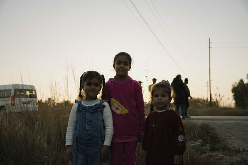 Free Three young girls stand together outdoors at twilight, showcasing a rural setting with warm tones. Stock Photo