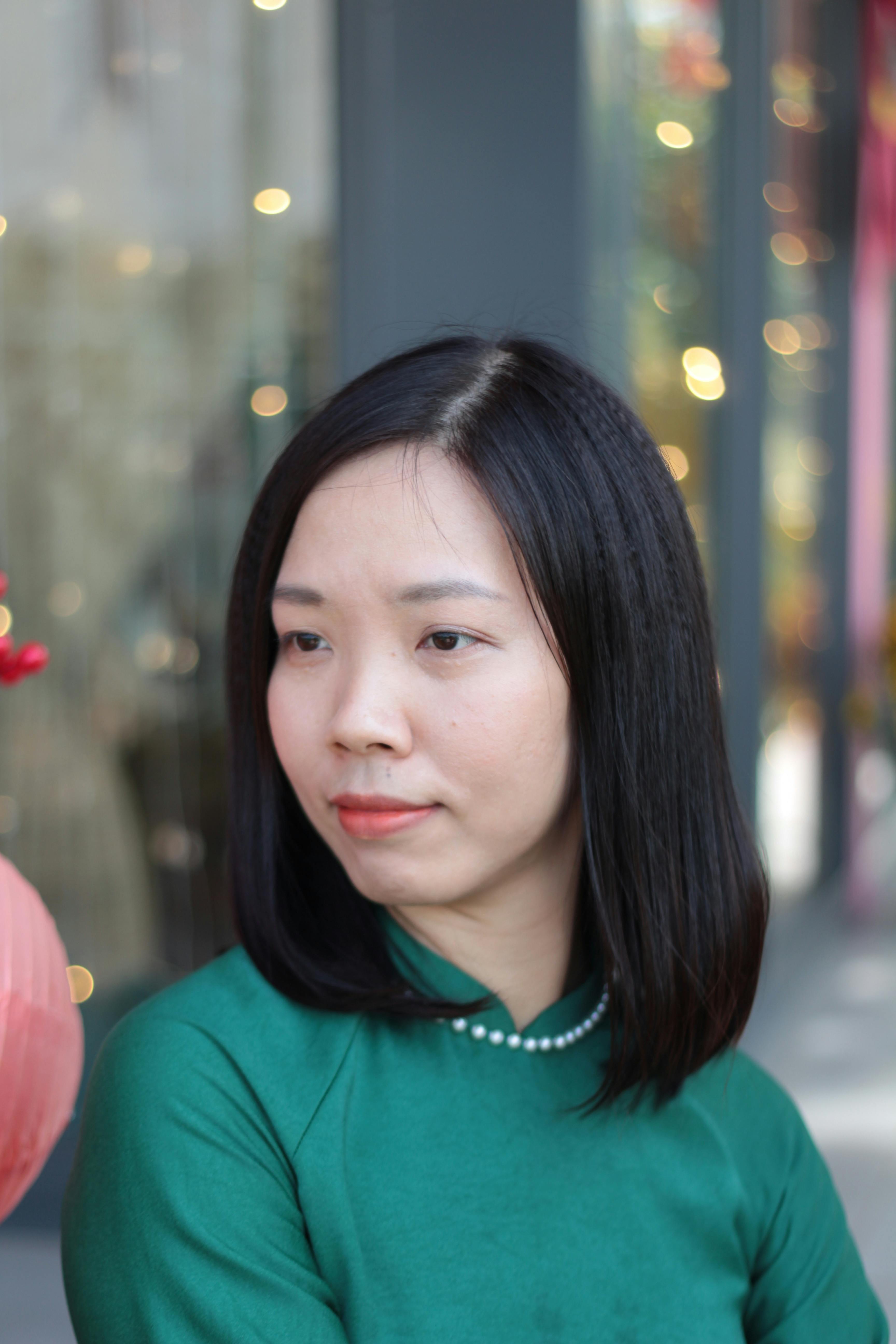 Portrait of a smiling woman in a green ao dai outdoors, enjoying a festive atmosphere.