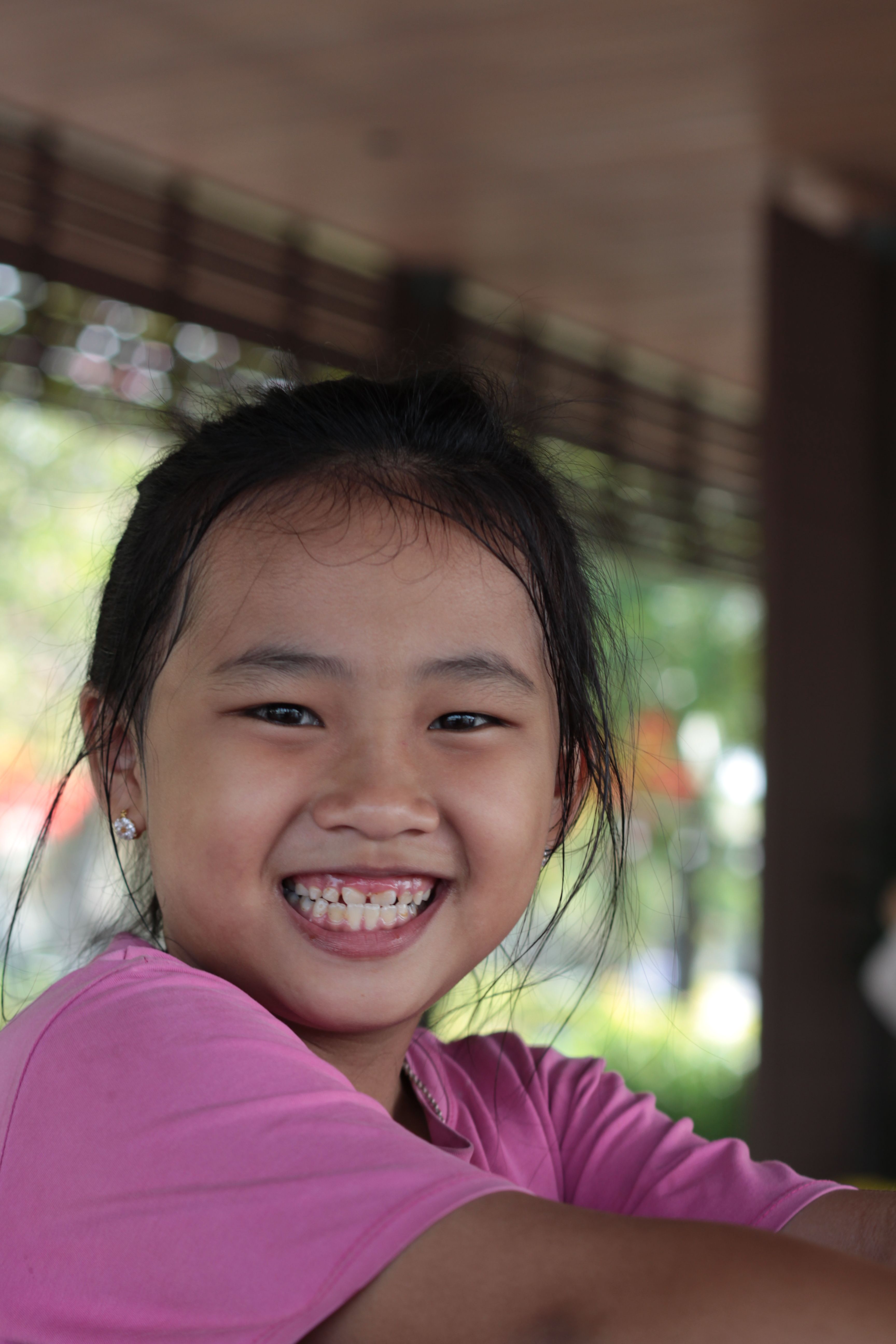 A cheerful child in pink clothing smiling broadly in an outdoor setting highlighting joy and positivity.