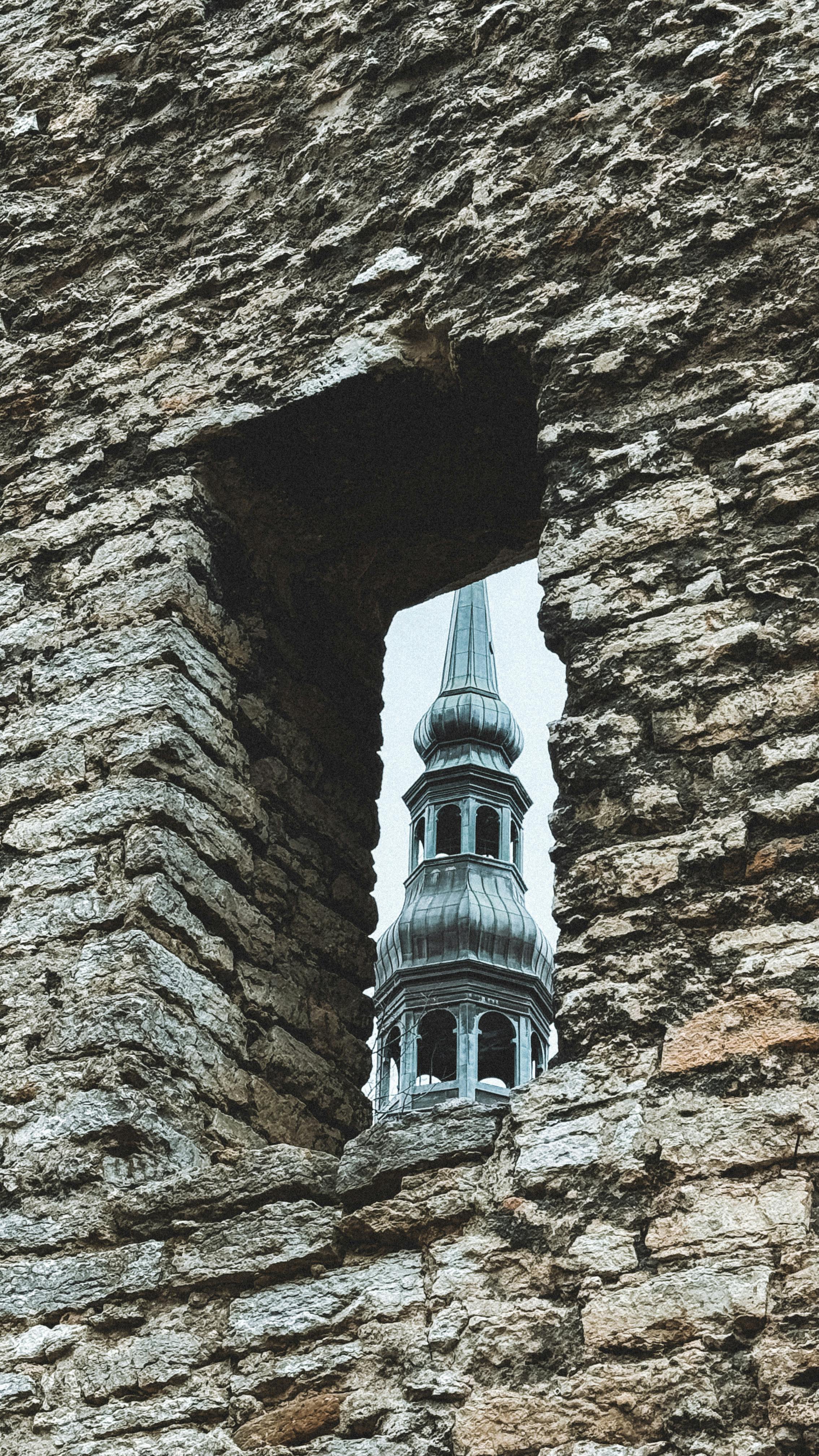 View of Tallinn's iconic tower framed by an ancient stone window, showcasing Estonia's historical architecture.